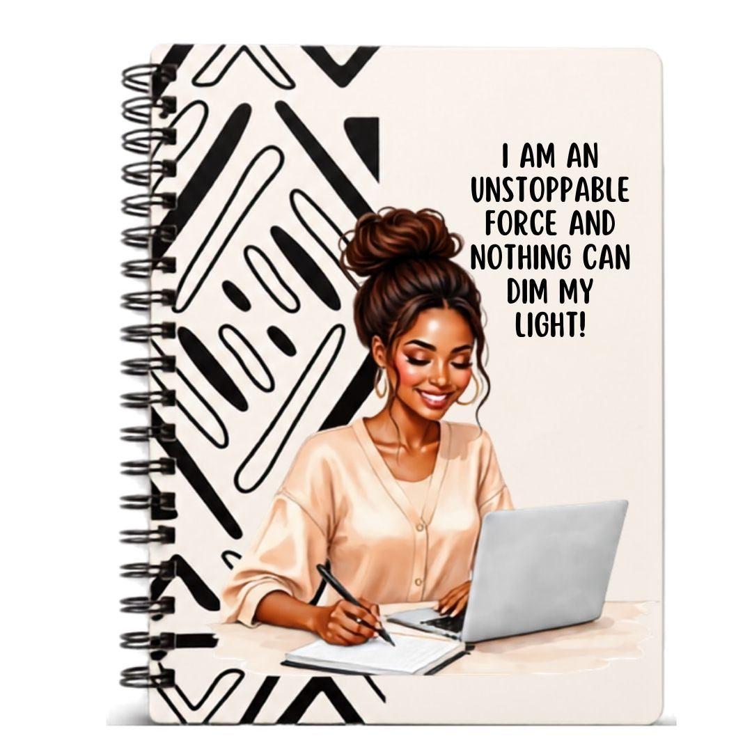 "A spiral-bound lined notebook with a black and white abstract patterned cover, featuring an illustration of a woman writing on a laptop with the text 'I AM AN UNSTOPPABLE FORCE AND NOTHING CAN DIM MY LIGHT!'."
